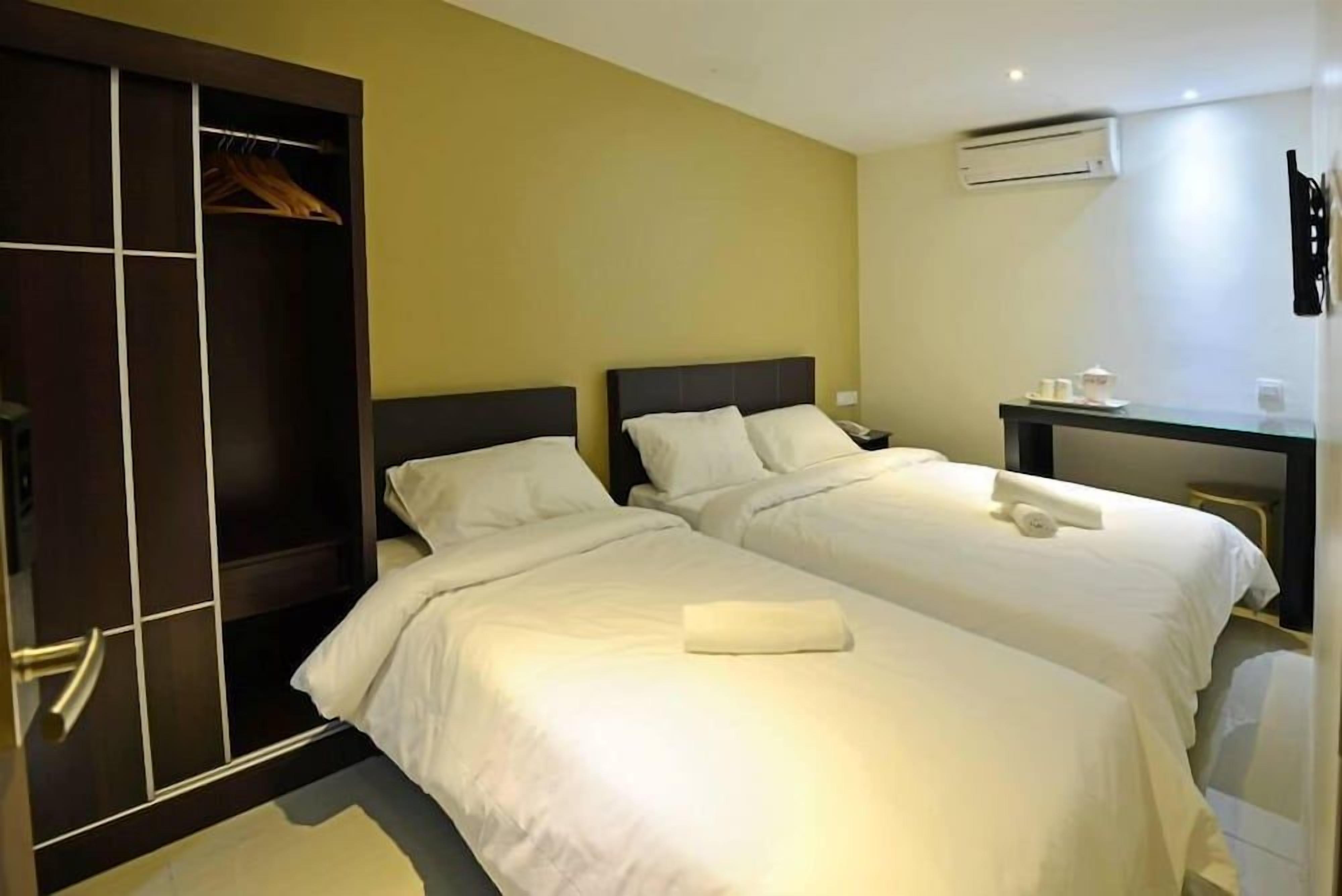 A hotel room with two beds, a wardrobe, a desk, and an air conditioning unit.