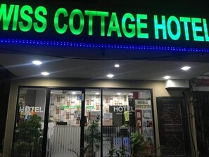 A hotel entrance with a neon sign reading 'MISS COTTAGE HOTEL' and glass doors.