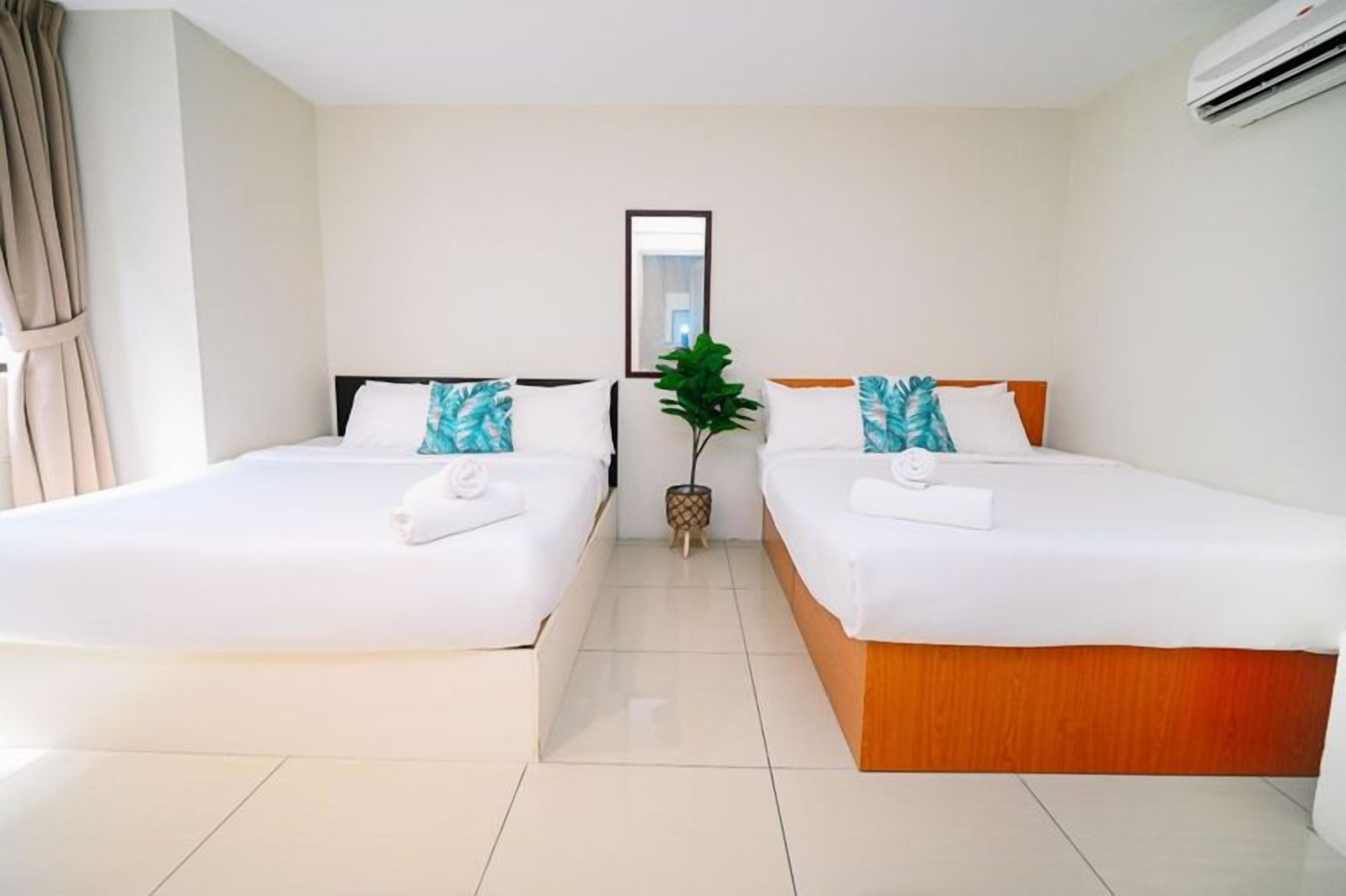 A hotel room with two single beds, a potted plant, and an air conditioning unit.