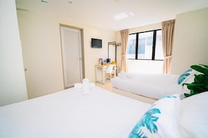 Ein Hotelzimmer mit zwei Betten, einem Schreibtisch mit Stuhl, einem Fernseher und einem Fenster mit Vorhängen.