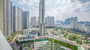 Um edifício alto com design moderno, cercado por outros edifícios altos e uma combinação de áreas verdes e infraestrutura urbana.