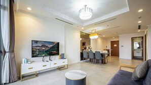 Uma sala de estar moderna com televisão de tela plana, um banquinho redondo, um sofá e um espaço de jantar com cadeiras e uma mesa.