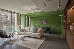A modern living room with a sofa, coffee table, and chairs. There is a dining area with a table and chairs. The room has large windows and a green accent wall. - Express by M Village Global City, a brand of Modern Village Lifestyle (Ho Chi Minh City)