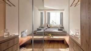 Un dormitorio moderno con un separador de vidrio, una cama con ropa de cama gris, una mesita de noche con una lámpara y una ventana con cortinas.