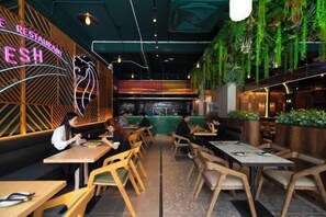 A restaurant interior with wooden tables and chairs, a neon sign, and hanging plants. - Express by M Village Global City, a brand of Modern Village Lifestyle (Ho Chi Minh City)