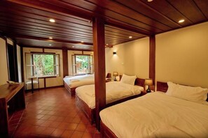 Une chambre d’hôtel avec trois lits, des poutres en bois au plafond et une vue sur la verdure environnante.