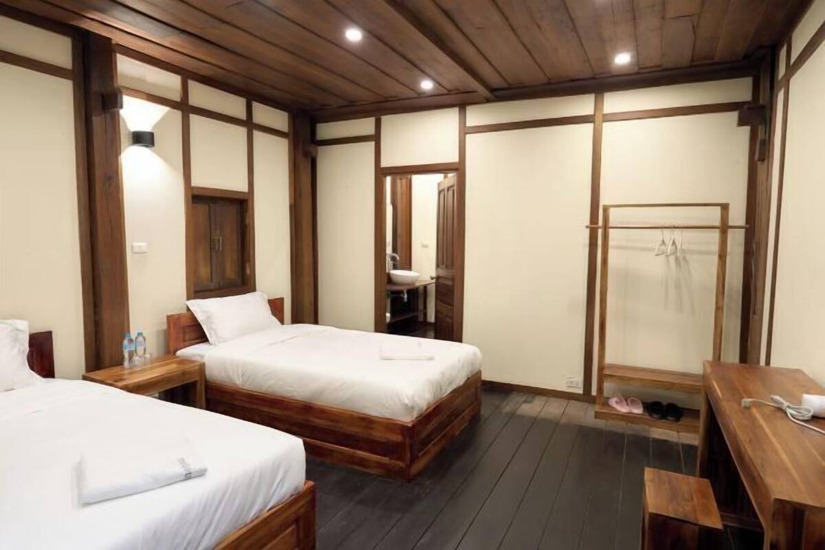 A bedroom with two wooden beds, a wooden desk, a mirror, and a wooden wardrobe.