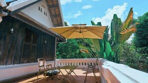 Eine Terrasse mit Tisch und Stühlen, einem gelben Sonnenschirm und Blick auf üppiges Grün.