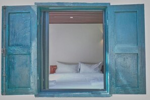 Une chambre avec un lit, une fenêtre dont les volets sont ouverts et une tête de lit en bois.