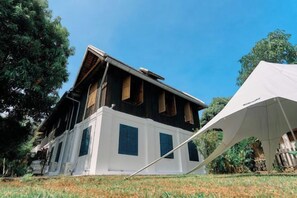 A two-story building with a white facade and dark wooden upper levels, surrounded by trees and a clear sky. - Fontainebleaulaos (Luang Prabang)