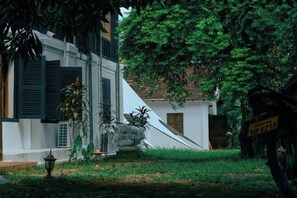 A building with a sloped roof, surrounded by greenery and a paved area. - Fontainebleaulaos (Luang Prabang)