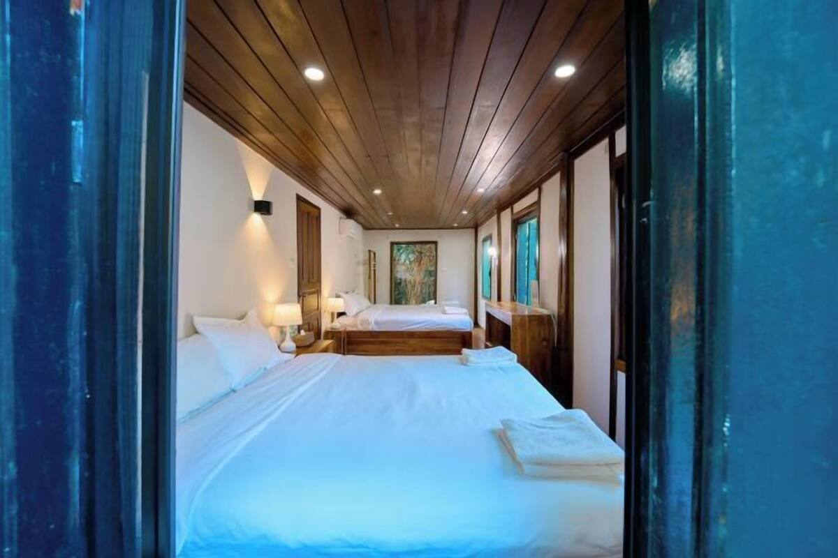 A hotel room with wooden ceiling, two beds, bedside tables, and a painting on the wall.