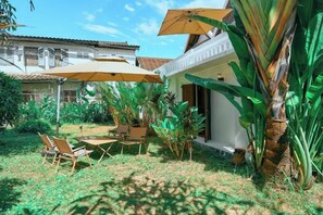 An outdoor patio with a table and chairs, surrounded by plants and umbrellas. - Fontainebleaulaos (Luang Prabang)