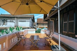Un balcon avec un parasol jaune, deux chaises et une table.