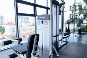Un gimnasio con equipamiento de ejercicio, amplias ventanas y vistas a edificios.
