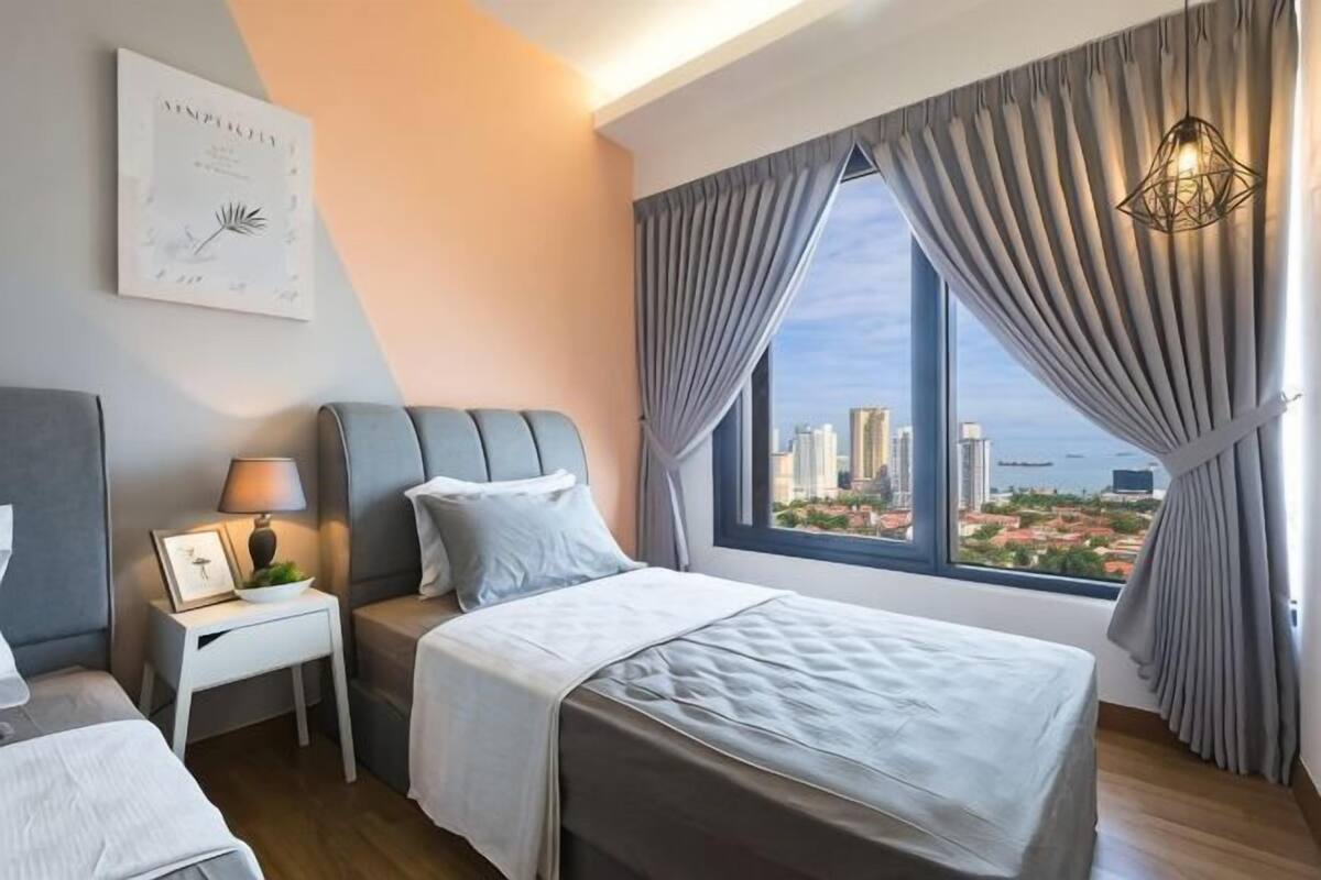 Une chambre d’hôtel avec un lit, une table de chevet, une lampe et une vue sur le paysage urbain, visible à travers de grandes fenêtres.