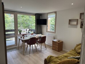 A room with a dining table set for two, a television mounted on the wall, and a bed with a yellow blanket.