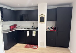 A modern kitchen with dark cabinetry, a built-in oven, a sink, and a coffee machine.