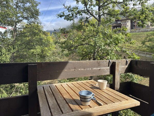 A wooden bench with a table, two mugs, and a spoon.