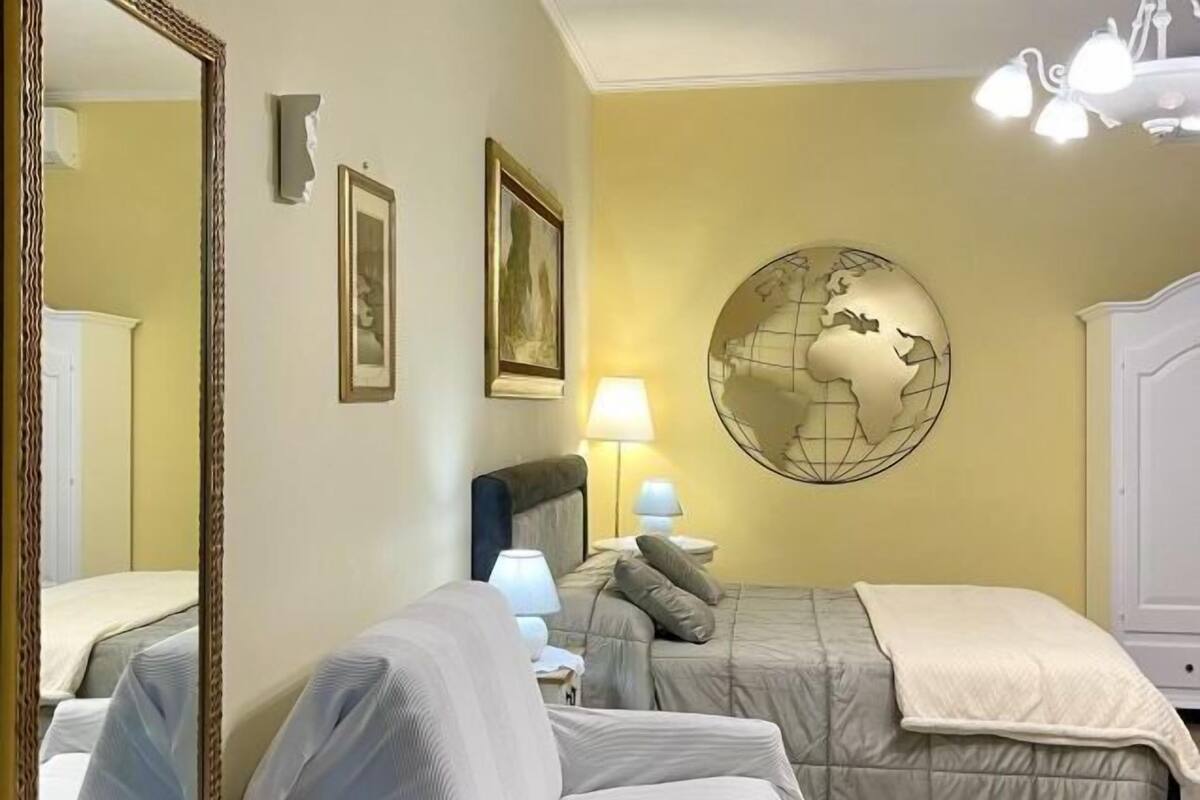Une chambre d’hôtel avec un lit, un grand miroir, deux tableaux encadrés, un globe décoratif et un lustre.