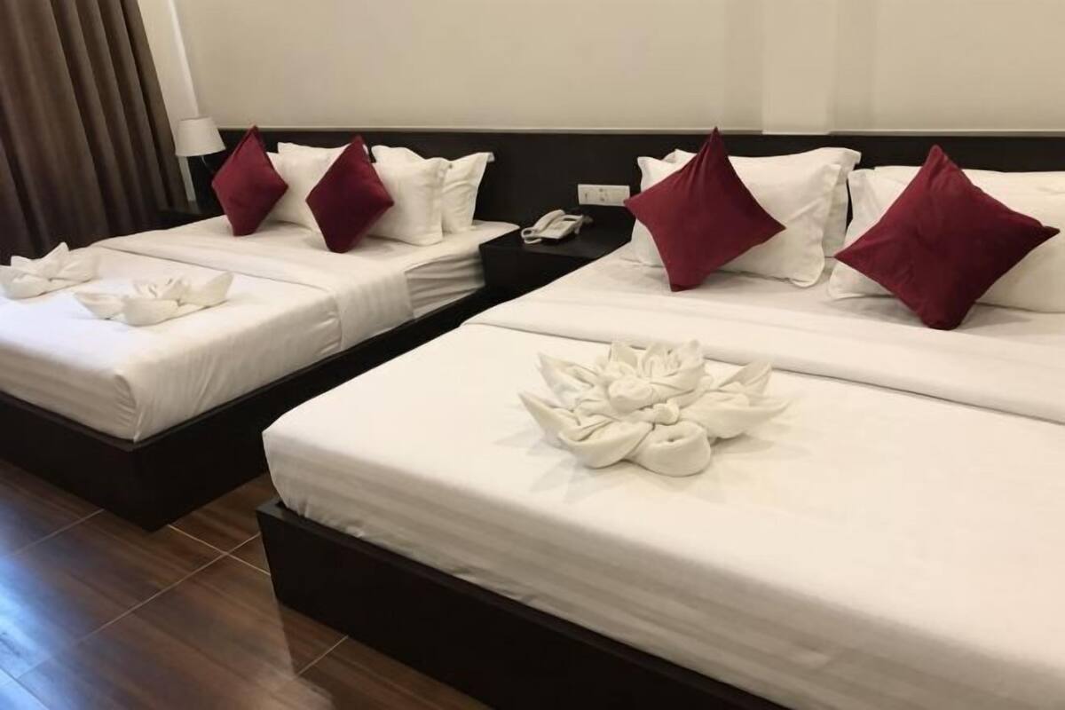 Two adjacent hotel beds with white linens, red pillows, and a neatly arranged towel on each bed.