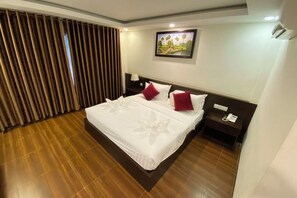 A hotel room with a large bed, wooden flooring, a nightstand with a lamp, and a painting on the wall. - Apple Hotel Two (Phnom Penh)