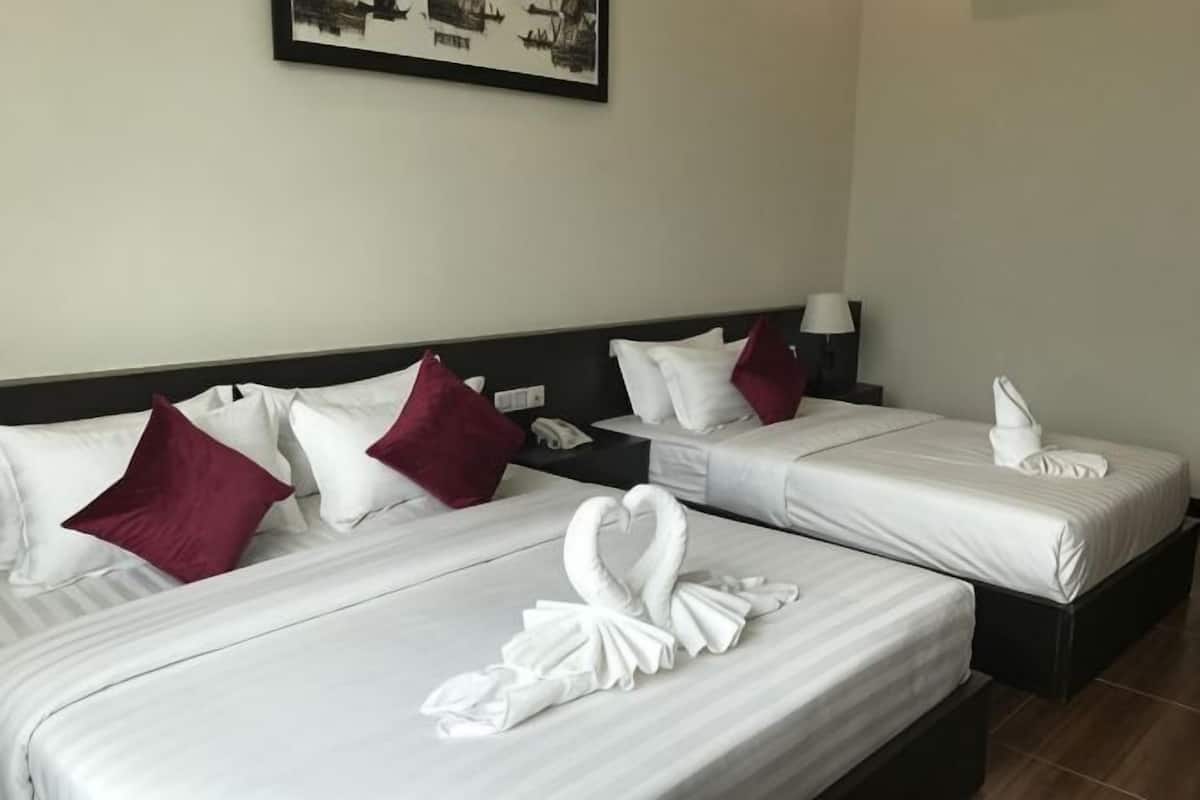 A hotel room with two beds, each with white linens and red pillows, a nightstand with a lamp, and a framed picture on the wall.