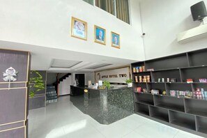 A hotel reception area with a marble counter, framed pictures on the wall, and a black shelving unit with various items. - Apple Hotel Two (Phnom Penh)