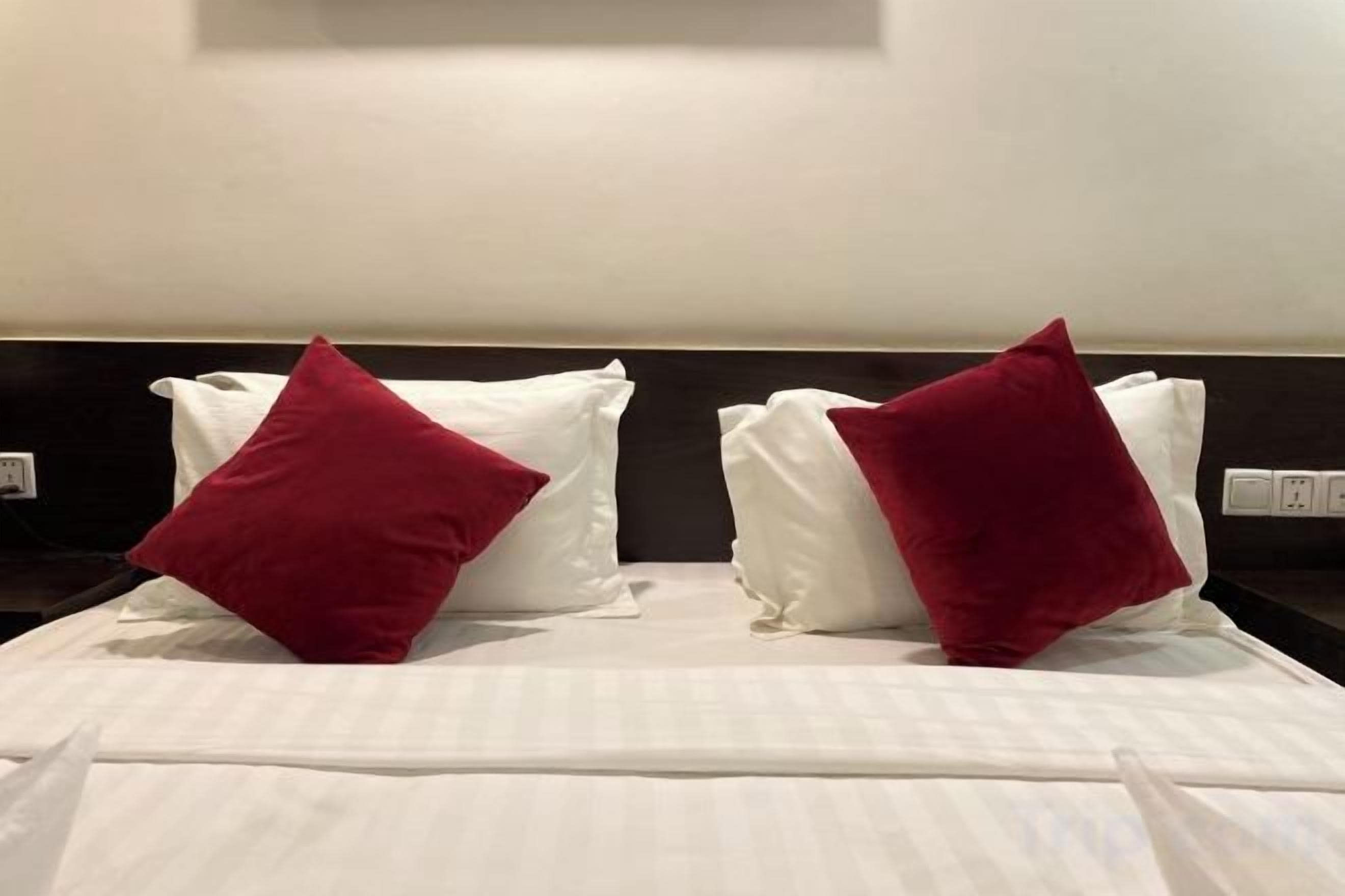 A bed with white linens and two red pillows.