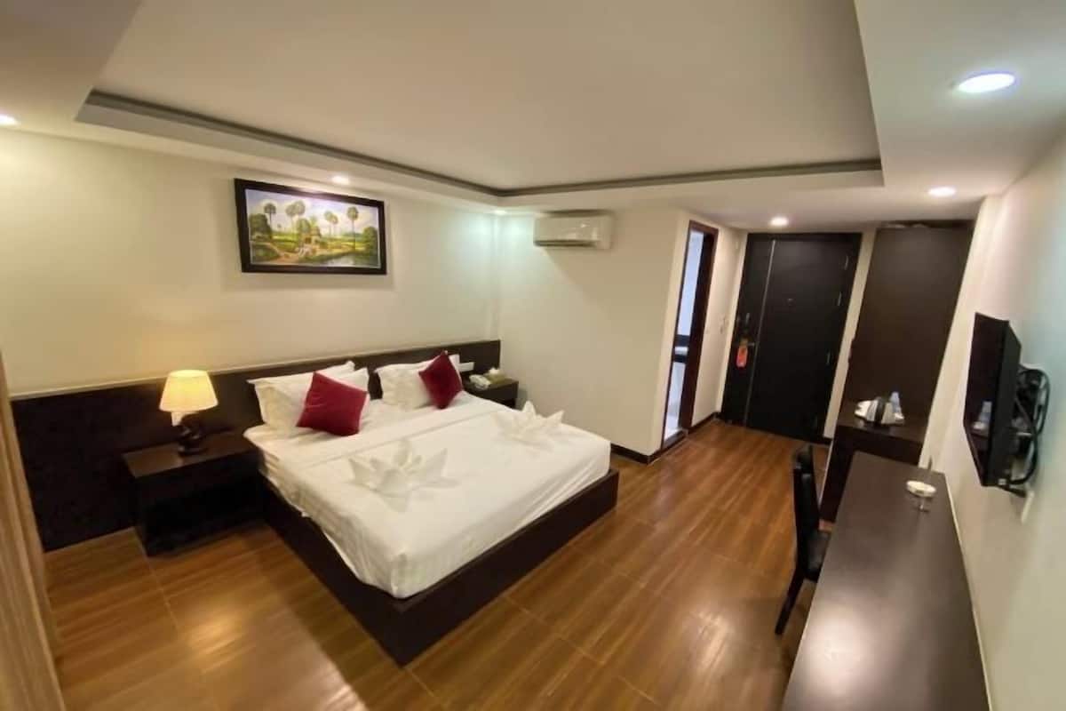 A hotel room with a large bed, a bedside table with a lamp, a painting on the wall, and a door leading to another room.