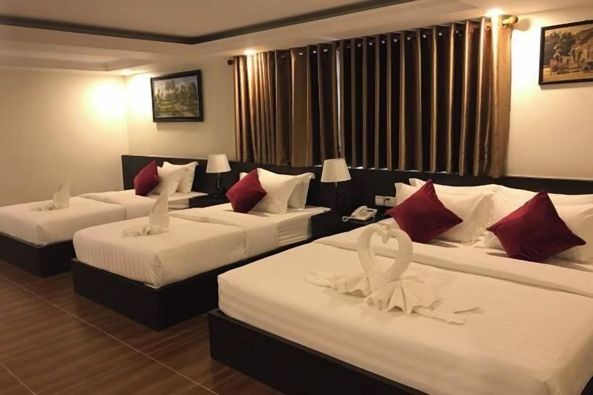 A hotel room with three beds, each with white linens and red pillows. There are bedside lamps and a telephone on the nightstands.