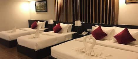 Ein Hotelzimmer mit drei Betten, jedes mit weißen Bettwäsche und roten Kissen. An den Nachttischen stehen Nachttischlampen und ein Telefon.