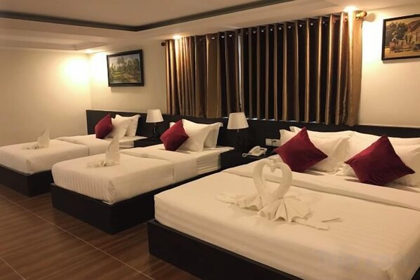 A hotel room with three beds, each with white linens and red pillows, a nightstand with a lamp, and a painting on the wall. - Apple Hotel Two (Phnom Penh)
