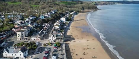 Un pueblo costero con playa, coches aparcados y edificios a lo largo de la costa.