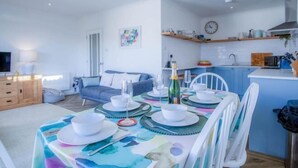 A dining area with a table set for four, a kitchen in the background, and a living room with a sofa and TV. - Footsteps - 2 Bedroom Apartment - Saundersfoot (Saundersfoot)