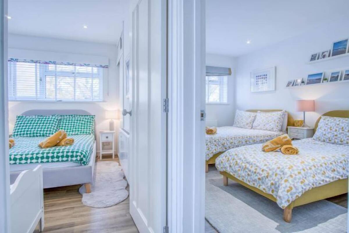 A bedroom with two beds, a white door, and a window with blinds.