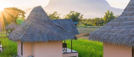 Thatched-roof huts with a view of a mountain and a field.