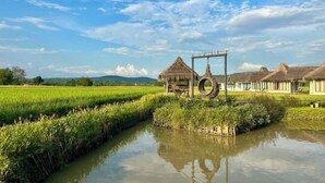 A rural landscape with a water channel, thatched-roof huts, and a clear sky. - Baan Porhdoi Goidao (Chiang Dao)