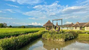 A rural landscape with a water channel, traditional thatched-roof structures, and a clear sky.