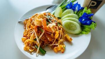 A plate of Pad Thai noodles with shrimp, bean sprouts, and a side of cucumber slices and lettuce.