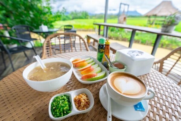 Une table avec un bol de soupe, une assiette de légumes coupés en tranches, une tasse de café décorée avec un motif en latte art, et des condiments.