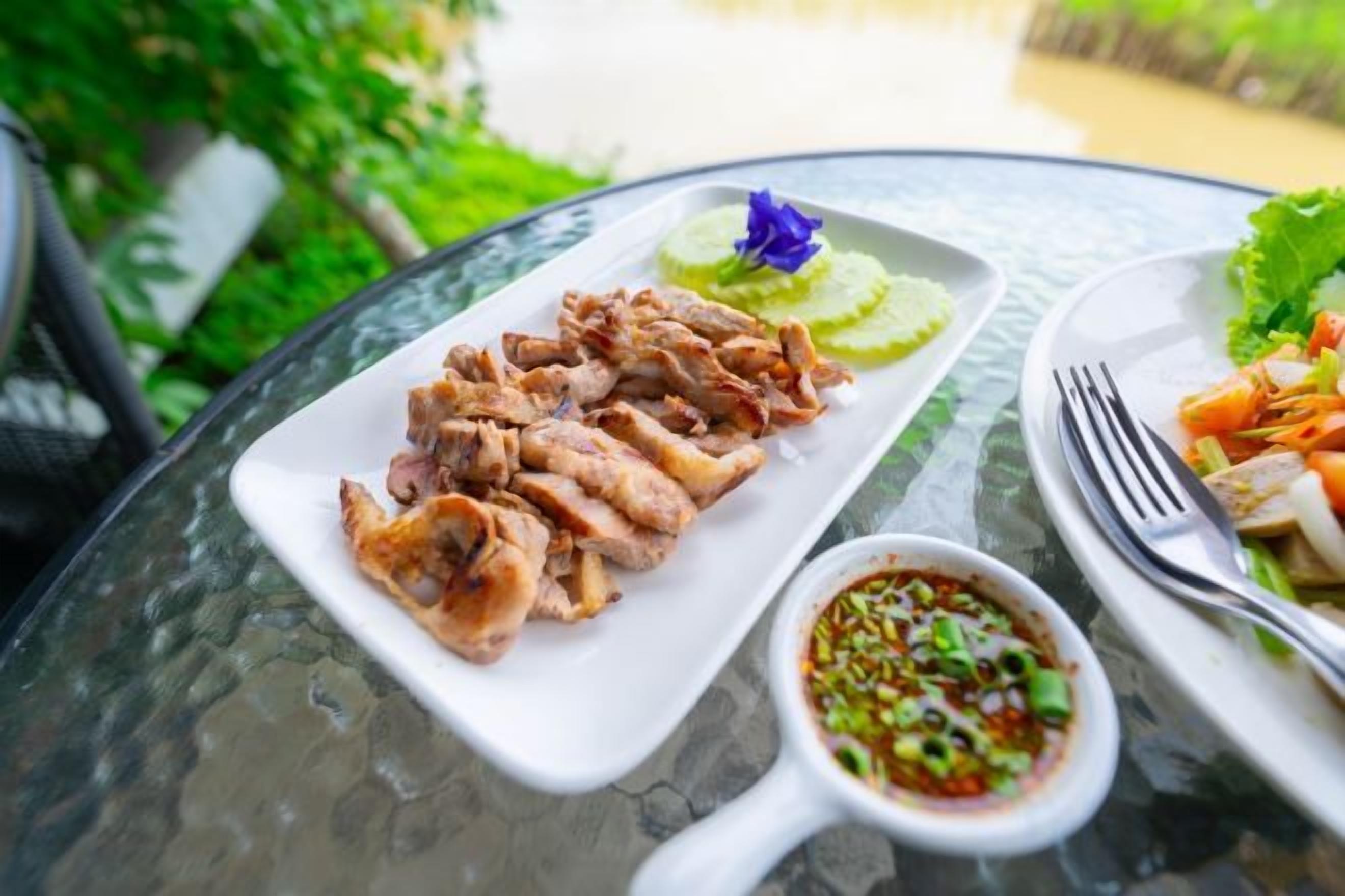 A meal with sliced meat, a small bowl of sauce, and a plate with vegetables on a glass table.