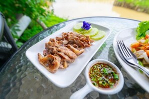 Un repas composé de viande tranchée, d’un petit bol de sauce et d’une assiette de légumes, le tout servi sur une table en verre.