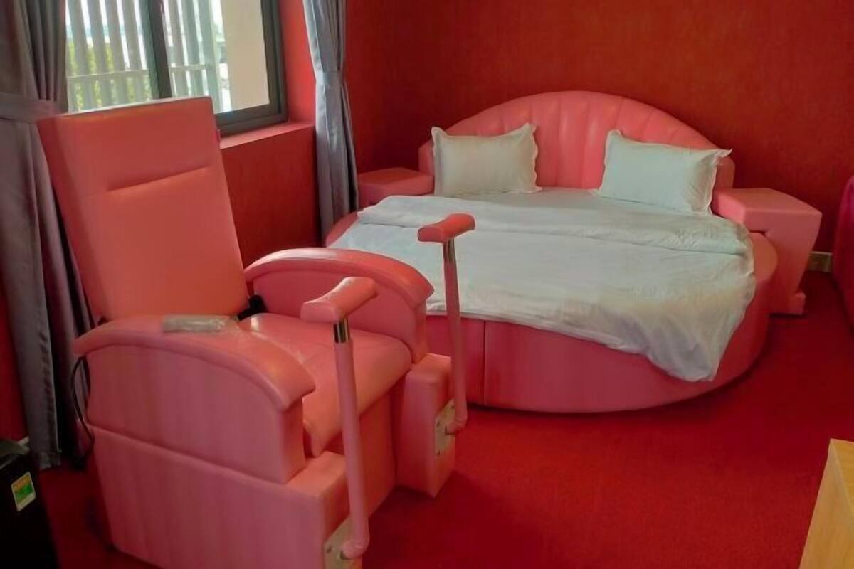 Un lit rose avec des oreillers blancs, une chaise rose et une petite table de chevet.