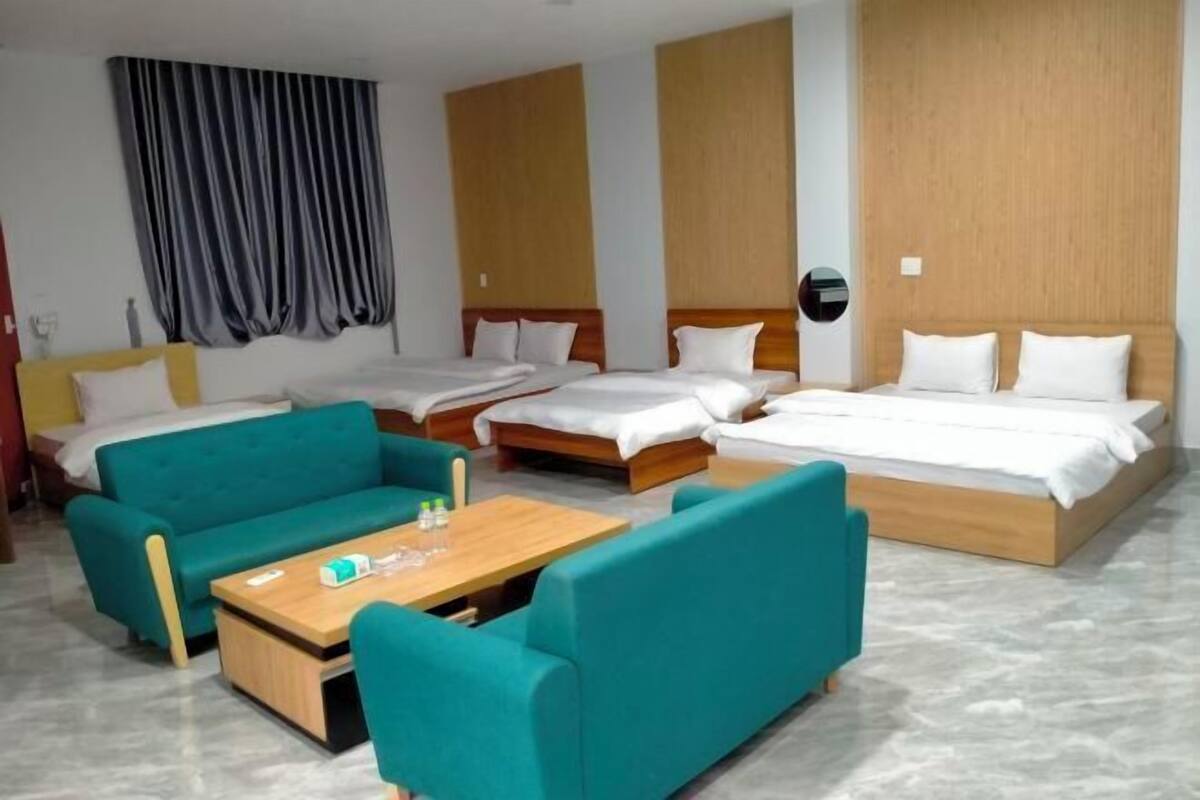 Une chambre d’hôtel avec deux lits simples, un canapé, une table basse et une grande fenêtre avec des rideaux.