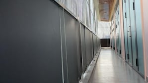 Un long couloir étroit, avec une série de portes d’un côté et un plafond élevé orné d’un motif en forme de grille.