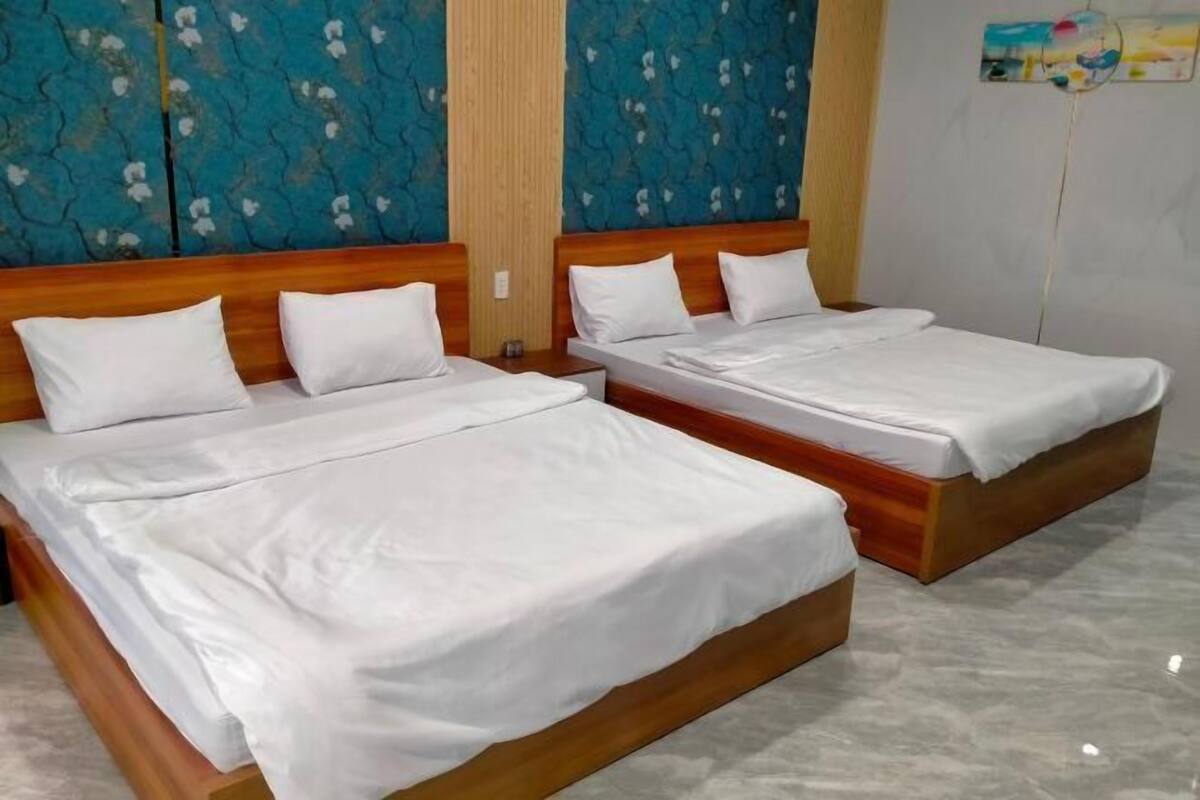 Deux lits côte à côte, avec des têtes de lit en bois, une literie blanche et un mur bleu à motifs derrière.