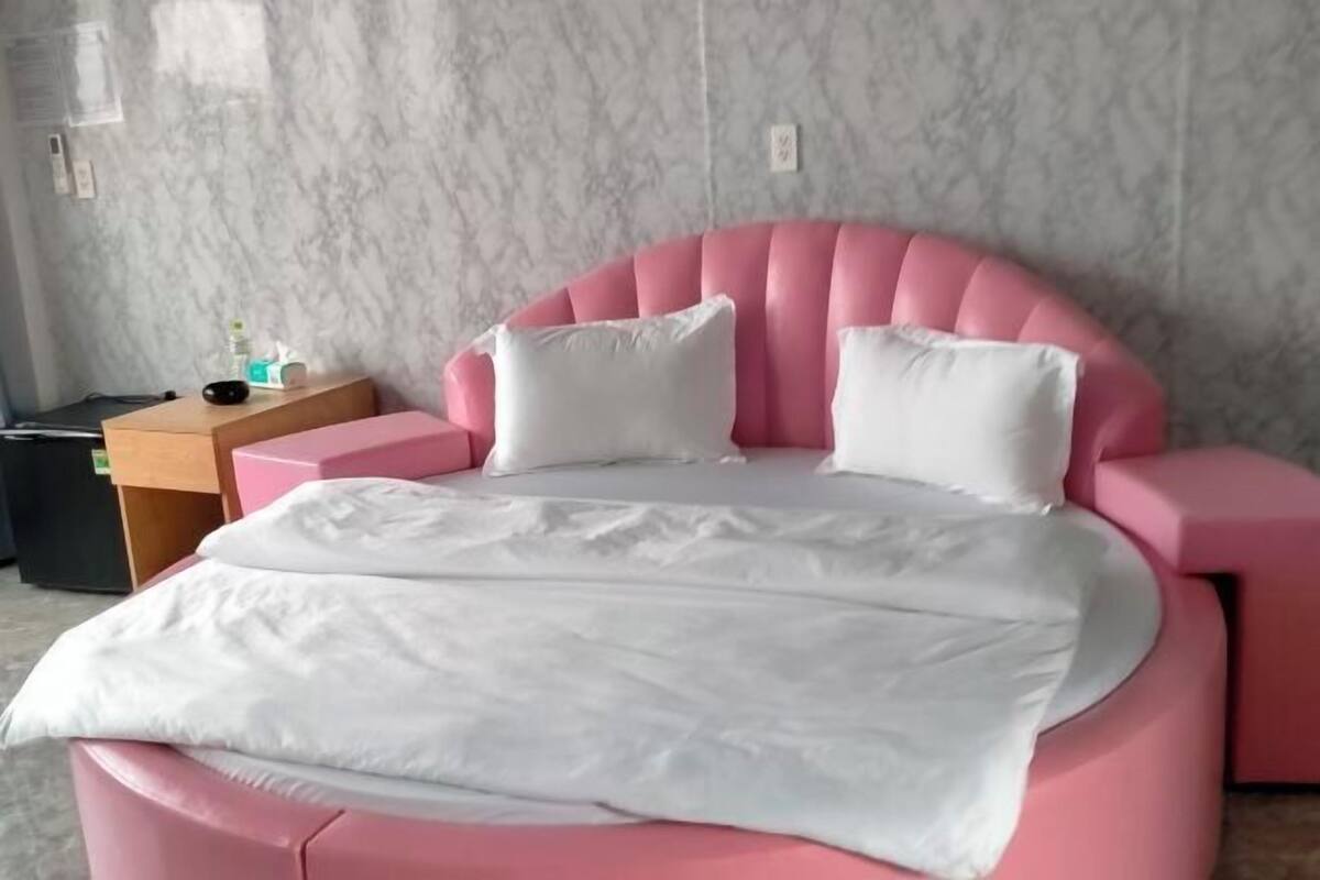Un lit rose avec une literie blanche, une table de chevet en bois et un mur en marbre.