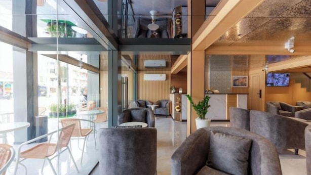 A modern hotel lobby with grey sofas, a glass partition, and a television. - Banana Guesthouse (Pattaya)