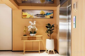 A reception area with a wooden console table, potted plants, and a painting on the wall. - Banana Guesthouse (Pattaya)